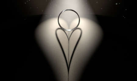 A single spotlight shining on a ring on a book castng a heart shaped shadow on a dark backgroundの写真素材