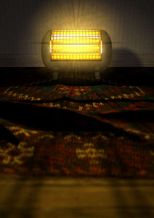 A cylindrical shaped electrical heater illuminated and radiating in an old room on a vintage red persian rug の写真素材