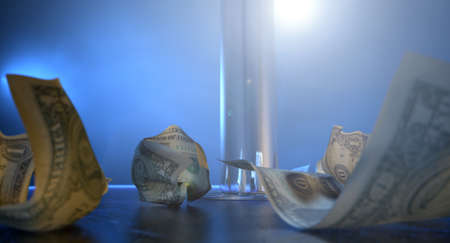 An isolated stripper pole on a stage lit by a single spotlight surrounded by crumpled up one dollar bill tips on a stripclub backgroundの写真素材