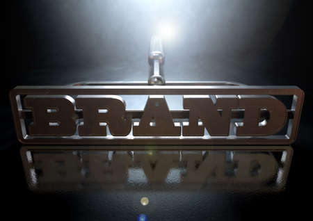 A metal cattle brand with the word brand as the marking area on an isolated dark backlit surface and backgroundの写真素材
