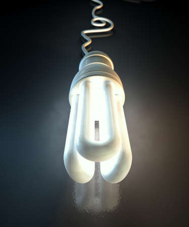 An illuminated fluorescent light bulb connected to an electical cable laying on a dark surface with...