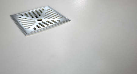 A closeup of a chrome shower drain set in on a white shower floor