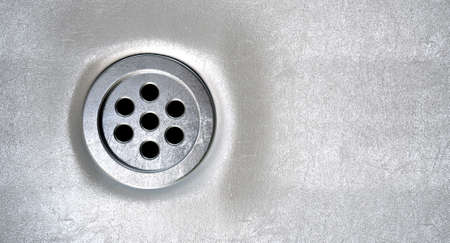 A closeup of a chrome plug hole set in a porcelain basinの写真素材