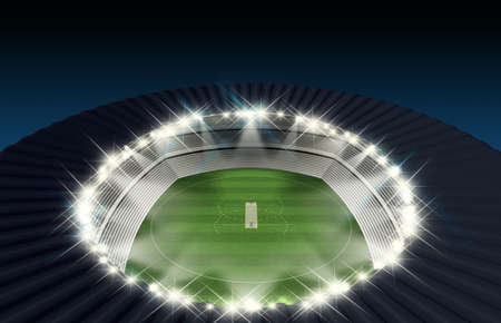 A cricket stadium with a pitch on a marked green grass field in the night time illuminated by an array of spotlightsの写真素材