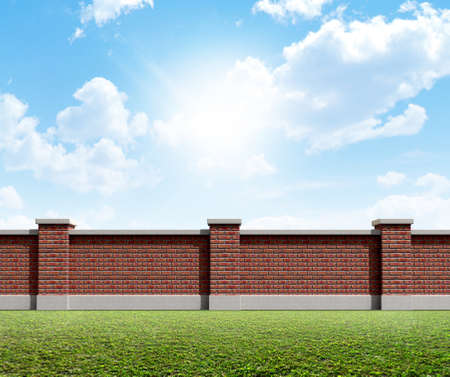 An front view of a regular domestic brick wall on a green grass and blue sky backgroundの写真素材
