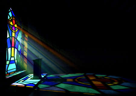 A dim old church interior lit by suns rays penetrating through a colorful stained glass window in the pattern of a crucifix reflecting colours on the floor and a speech pulpitの写真素材