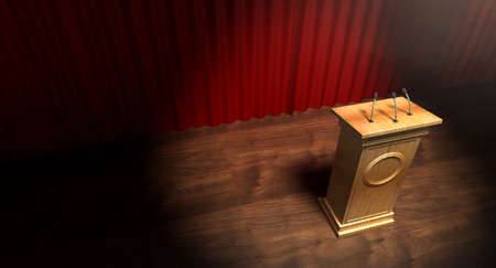 A regular theater stage with closed red curtains and a wooden debate podium lit by a single spotlightの写真素材