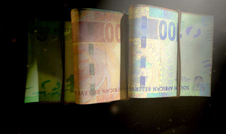 A close-up view of three wads of folded over stacks of south african banknotes each bound infomally...