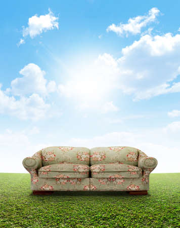A green and pink floral sofa outside on a perfect flat green lawn against a blue sky with white cloudsの写真素材