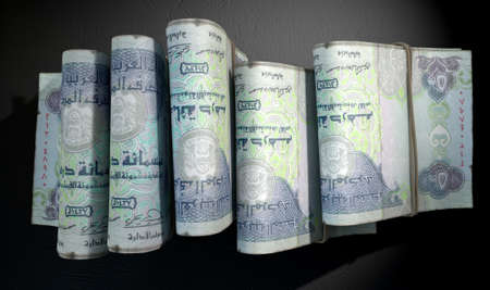 A close-up view of five wads of folded over stacks of dirham banknotes each bound infomally by a rubber band set out in a domino formation on an isolated dark studio backgroundの写真素材