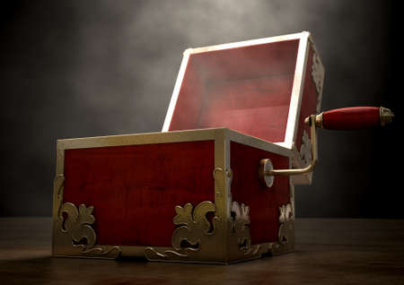 An ornate antique open jack-in-the-box mad of red wood and gold trimmings on a dark studio background under a spotlightの写真素材