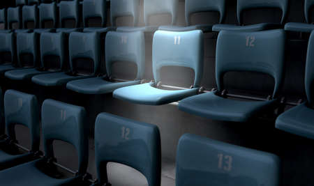 A section of numbered stadium seating set in rows oin the dark with one seat  being singled out by a spotlightの写真素材