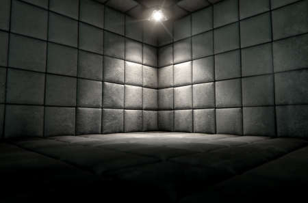 A dark dirty white padded cell in a mental hospital with a corner lit by a single spotlightの写真素材
