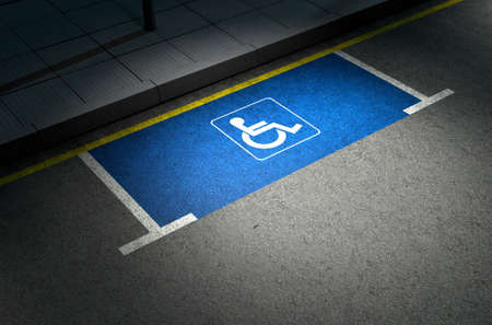 A section of a tarmac road with an empty demarcated paraplegic parking area at night lit by a street pole lightの写真素材