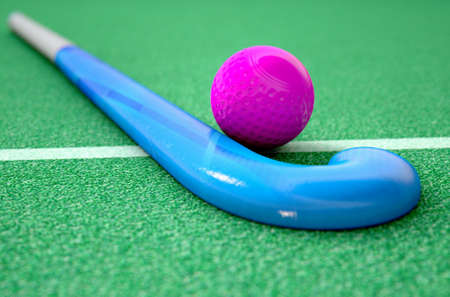 A 3D rendering of a hockey stick and ball on green artificial grass in the daytimeの写真素材