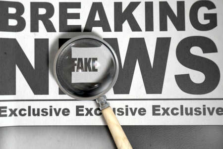 A fake news concept showing a printed newspaper with a magnifying glass highlighting an underlying...