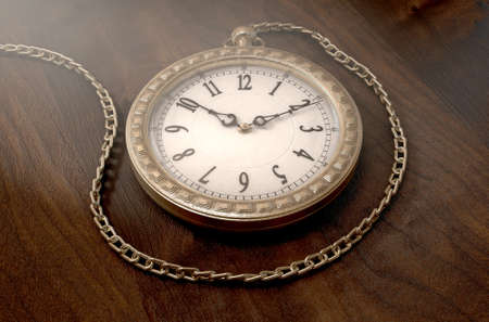 A closeup of an intricate gold antique pocket watch attached to a chain on a wooden surface background - 3D renderの写真素材