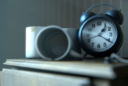 A real life concept scene showing a vintage clock on a bed side table with dirty coffee mugs and a stained top at night - 3D Renderの写真素材