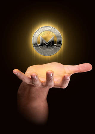 A male hand conjuring up a floating monero cryptocurrency hologram in gold and silver physical coin form on a dark studio backgroundの写真素材