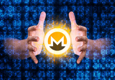A pair of male hands reaching through digital numerical data figures grasping at a monero coin hologramの写真素材