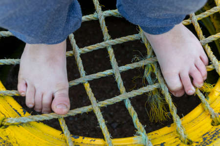 A Small boys feet standing on top of a yellow tire with netting sowen into the middleの写真素材