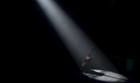 An acoustic guitar resting on a stand on a music concert stage lit by a single dramatic spotlight on...