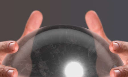 A close up of a pair of male hands surrounding a crystal ball on an isolated dark studio backgroundの写真素材