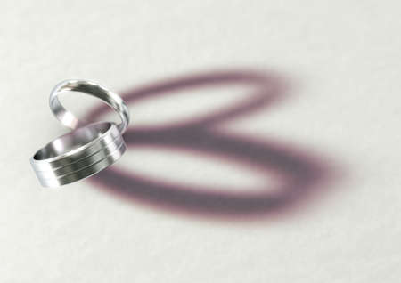 A pair of white wedding rings resting on an isolated white suface casting a shape resembling a heart - 3D renderの写真素材
