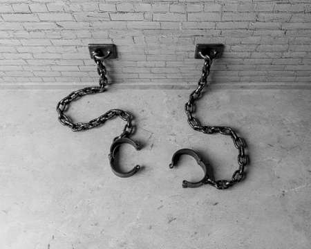 A set of empty old iron shackles draped on the floor connected to an isolated white brick wall  - 3D renderの写真素材