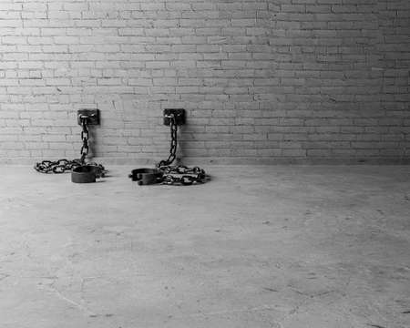 A set of empty old iron shackles draped on the floor connected to an isolated white brick wall  - 3D renderの写真素材