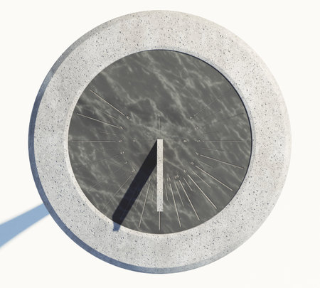A modern round stone sundial with etched roman numerals standing an a monolithic rock base on an...