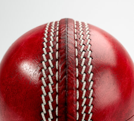 A regular red cricket ball with white stitching and generic gold branding on an isolated background - 3D renderの写真素材