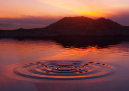 A sunset and mountain reflecting over a smooth lake with a water ripple - 3D renderの写真素材