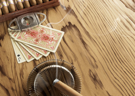 A scene with a set of cigars and antique playing cards and a lit cigar in an ashtray on a wooden surface - 3D renderの写真素材