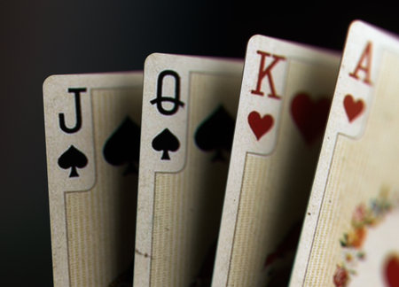 Closeup image of four vintage playing cards featuring jack, queen, king, and ace on a dark...