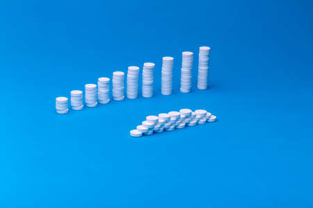 Close up pyramid concept of white pills on blue background with copy space. Focus on foreground,...