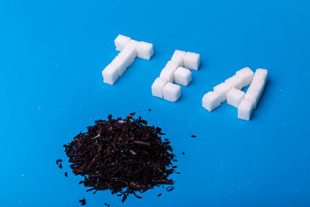 tea leaves and sugar cubes are laid out in the form of the inscription tea on a blue background....