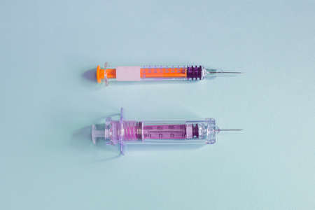 Two different vaccination syringes with the needle uncapped on a textured blue paper background. Health sciences and medicine.の写真素材