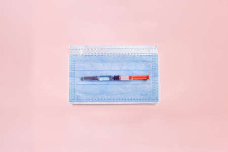 A pre-filled syringe with a ready-to-use medical solution rests on a small surgical mask for children on top of a textured pink paper background. Health sciences and medicine.の写真素材