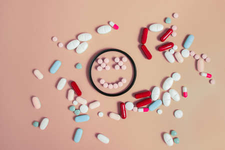 Smiley face made up of pills on a pastel orange table with some other scattered medications.