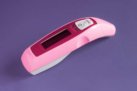 Ear and forehead laser pink thermometer for families on a colorful studio background. Medicine and...