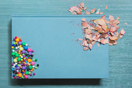 Blue hardcover book stained with colored pencils shavings and some thumbtacks on a wooden school...