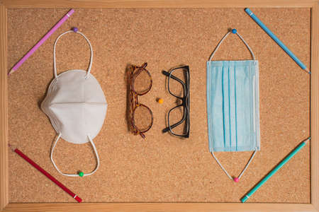 Corkboard with four colored pencils in the corners with a different pair of lenses and two masks to protect and limit the spread of COVID-19. Glasses for adults and children. Back to school concept.の写真素材