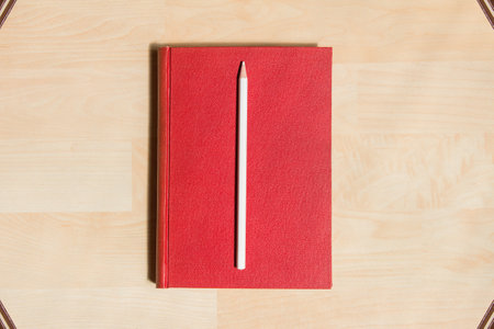 White pencil in a red hardcover on a parquet background and some books in the corners as a frame.の写真素材