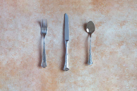 Overhead view of an antique silver cutlery consisting of a fork, spoon, and knife on an abstract background and ceramic texture with pastel color. Antiques and metals.の写真素材