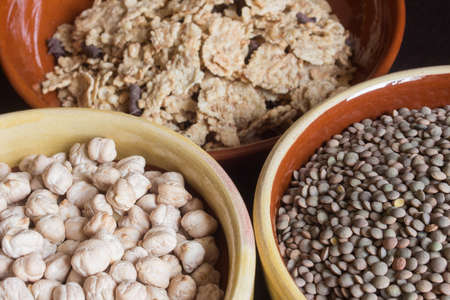 Close-up of a bowl of chickpeas, another of lentils with an unfocused background of cereals.