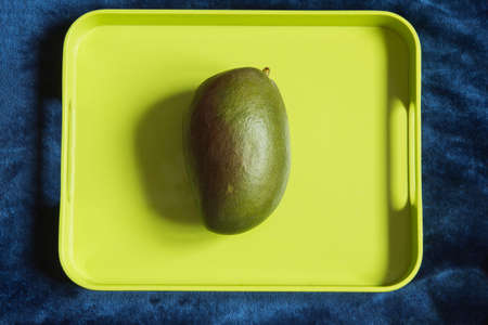 A large green mango on a colorful tray with space to input a text. Tropical fruit and food.