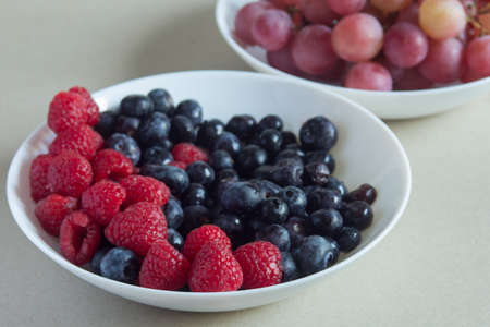 A close-up of a few raspberries in several plates with fruits of the forest on a textured surface. Natural ingredients and healthy food.の写真素材