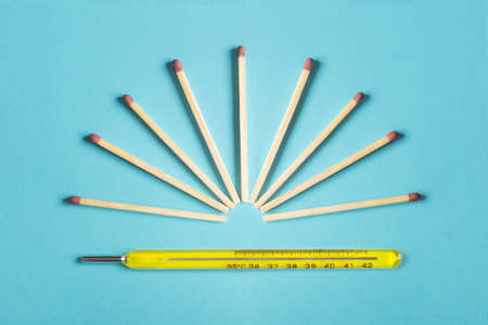 A group of matches ready to light forming a sun on top of a hot mercury thermometer on a colorful...