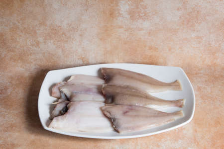 Megrim fishes on a white font with a textured abstract studio background. Healthy fresh food.